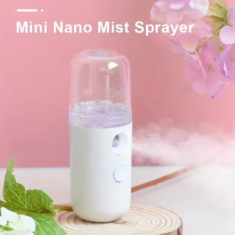 Portable Sprayer - White mini nano mist sprayer with clear transparent top cap, resting on a wood slice against a pink background with flowers nearby