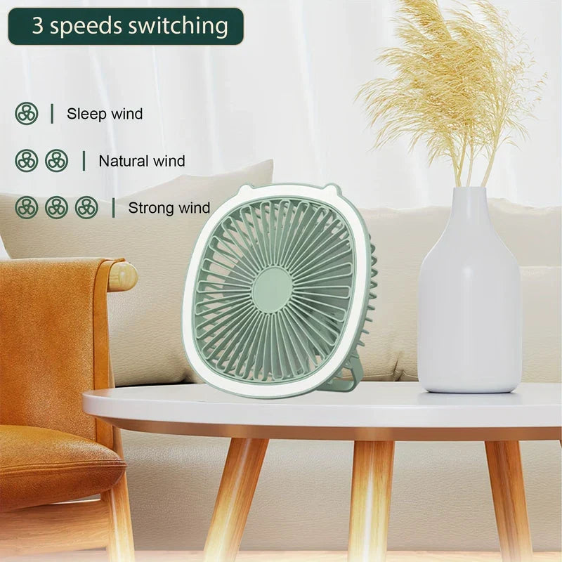 Compacto ventilador de escritorio verde sobre una mesa redonda blanca junto a un jarrón de hierba de la pampa, con tres modos de velocidad etiquetados