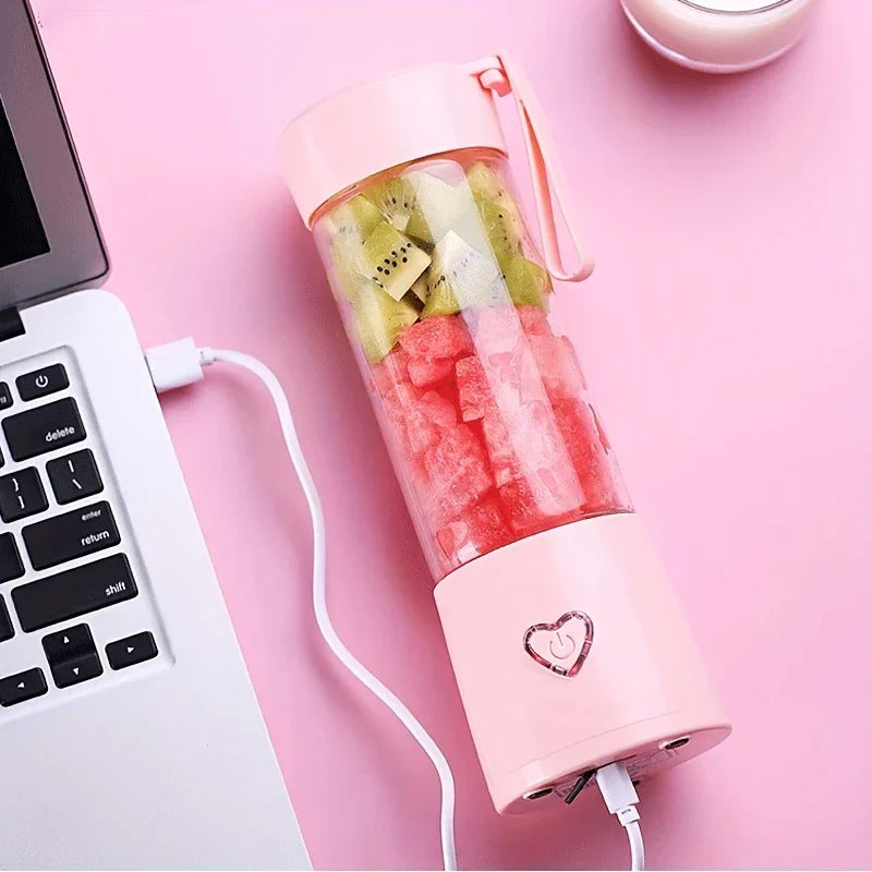 عصارة محمولة - خلاط محمول وردي بداخله قطع كيوي وبطيخ، أثناء الشحن عبر كابل USB بجوار كمبيوتر محمول