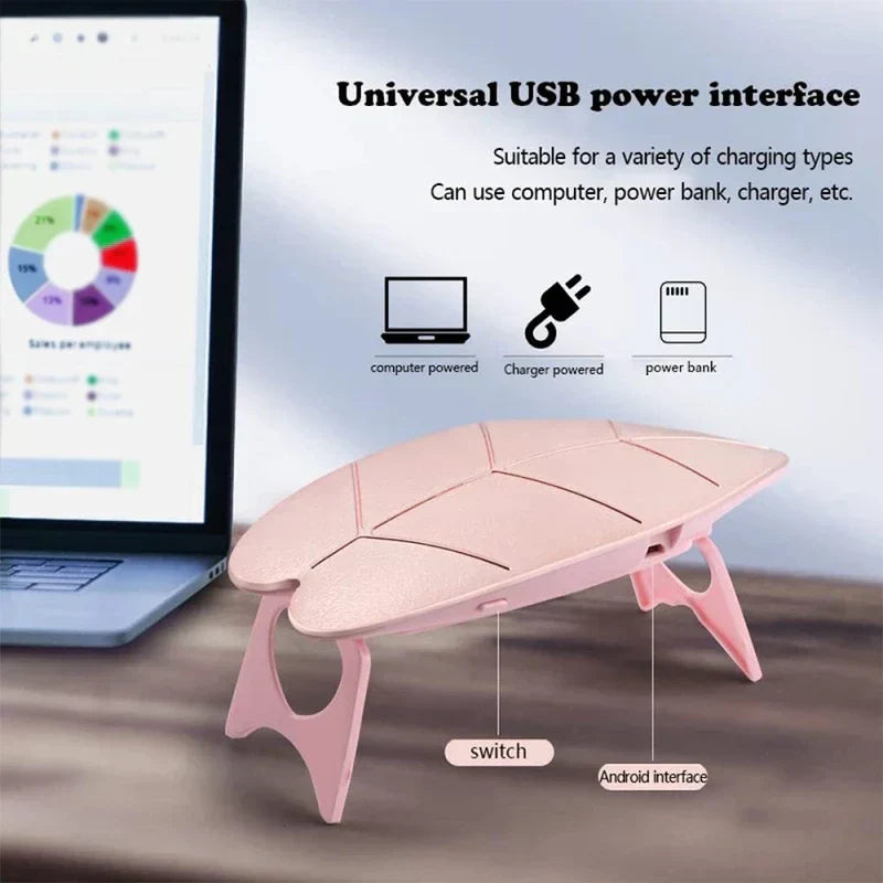 مصباح أظافر uv led - جهاز وردي على شكل ورقة شجر يستند إلى أرجل قابلة للطي بجانب حاسوب محمول، مع توضيح لمفتاح التشغيل ومنفذ شحن USB.