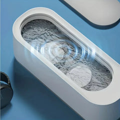 Top view of an open eyeglass cleaner machine with water inside, next to a watch on a blue surface