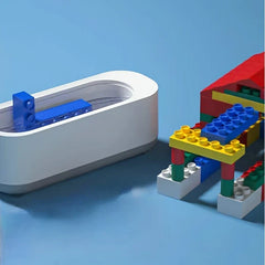 White eyeglass cleaner machine with blue building blocks inside, next to a colorful block structure on a blue background