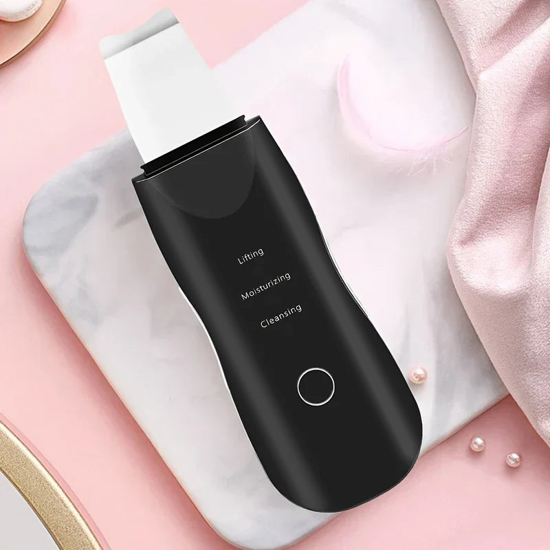 Skin Scrubber Spatula - Black handheld skincare device resting on a marble tray with pink soft styling accents