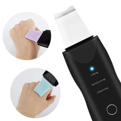 Espátula exfoliadora de piel: espátula exfoliadora ultrasónica negra con tres modos etiquetados, mostrada con dos accesorios intercambiables de silicona texturizada sobre la piel