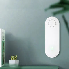 White wall-mounted ultrasonic pest repeller with top power button and green indicator, beside a small potted succulent and book