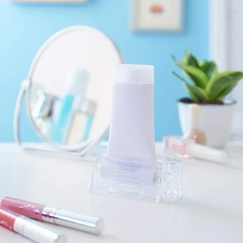Wall Mount Toothpaste Dispenser - Clear tube squeezer holding a white skincare tube, placed on a white vanity table with cosmetics and a mirror in the background