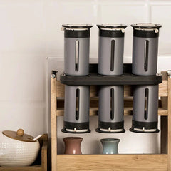 Magnetic Spice Rack Shelf - Rack with six gray and black spice canisters placed on a light wood kitchen shelf next to a ceramic lidded jar and small ceramic vases