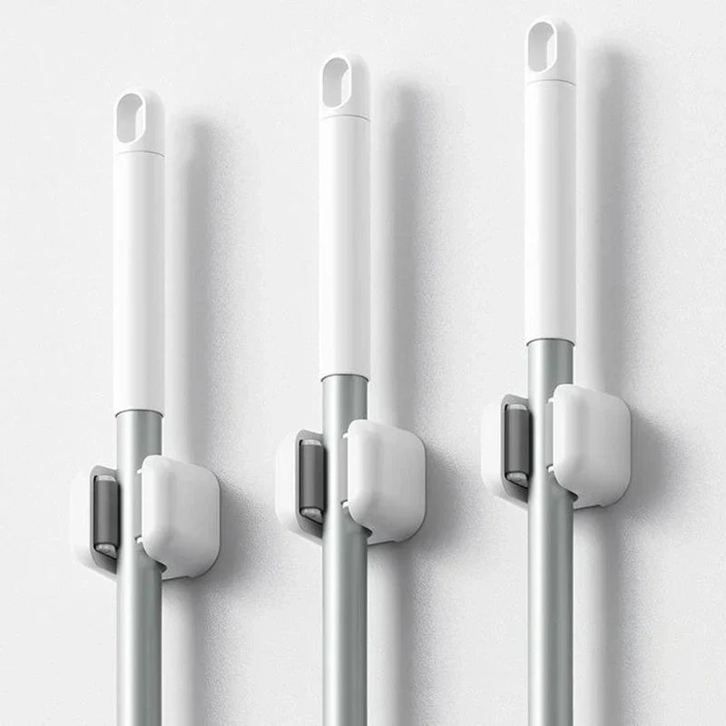 Broom Holder - Three identical white grip clips mounted on a white wall, each holding a long silver and white cleaning tool handle