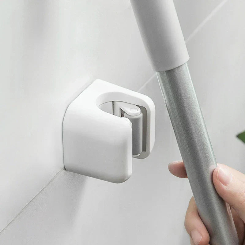 Broom Holder - Hand positioning a silver and white cleaning tool handle into an installed white wall grip clip at a tiled wall corner