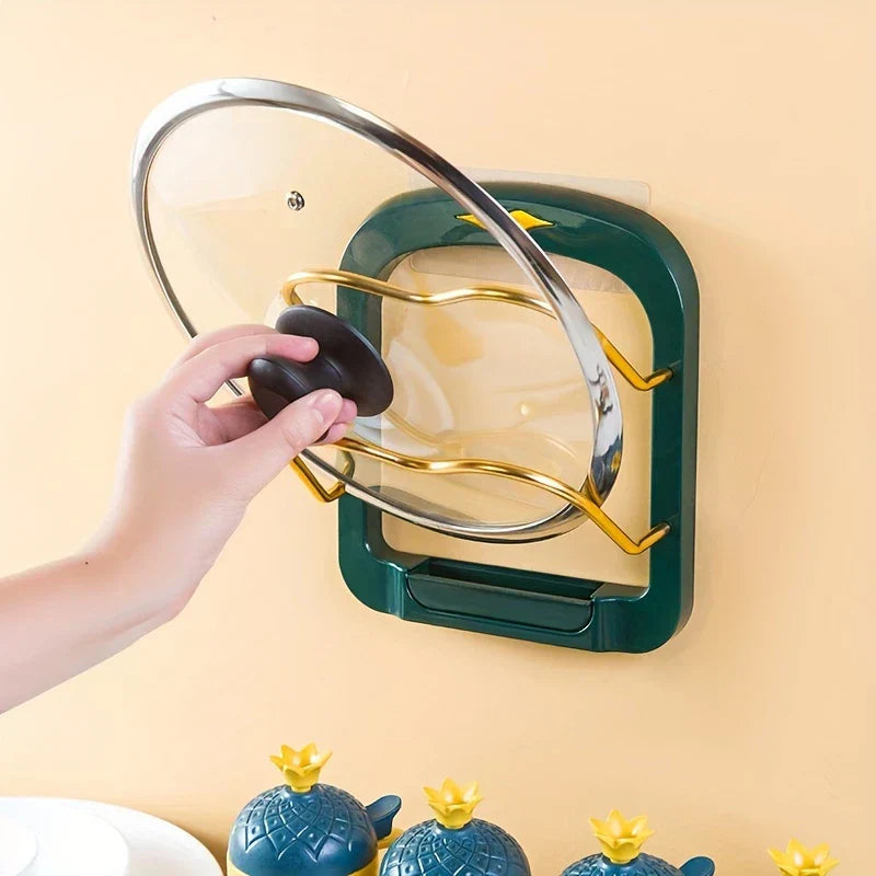 Pot Lid Organizer - Hand placing a glass lid onto a dark green wall-mounted lid organizer, with small blue pineapple-shaped containers below