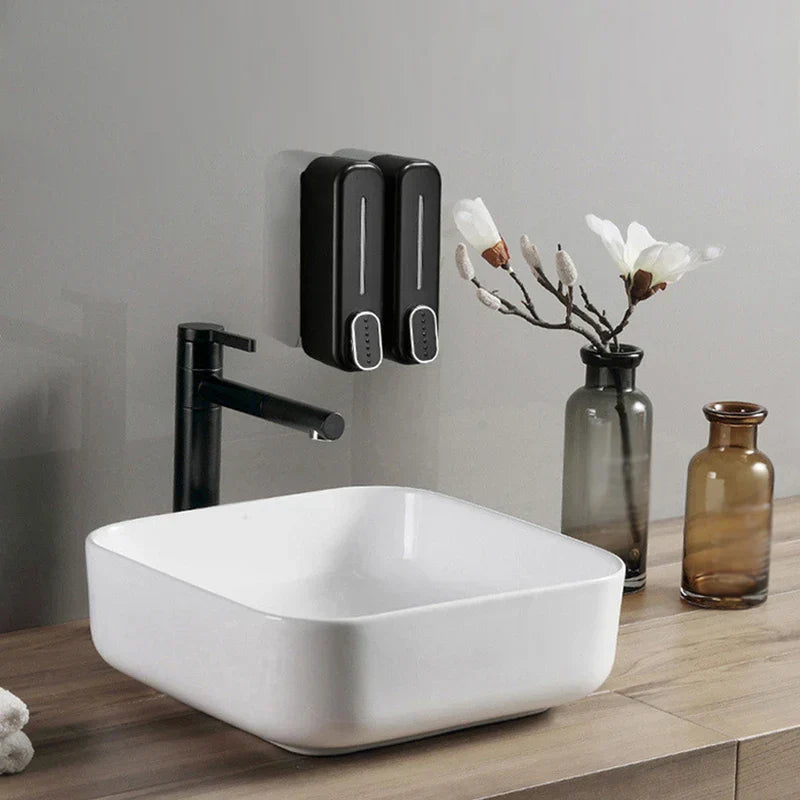 Soap Shampoo Dispenser - Two black wall-mounted soap shampoo dispensers beside a bathroom sink with faucet and decorative vases
