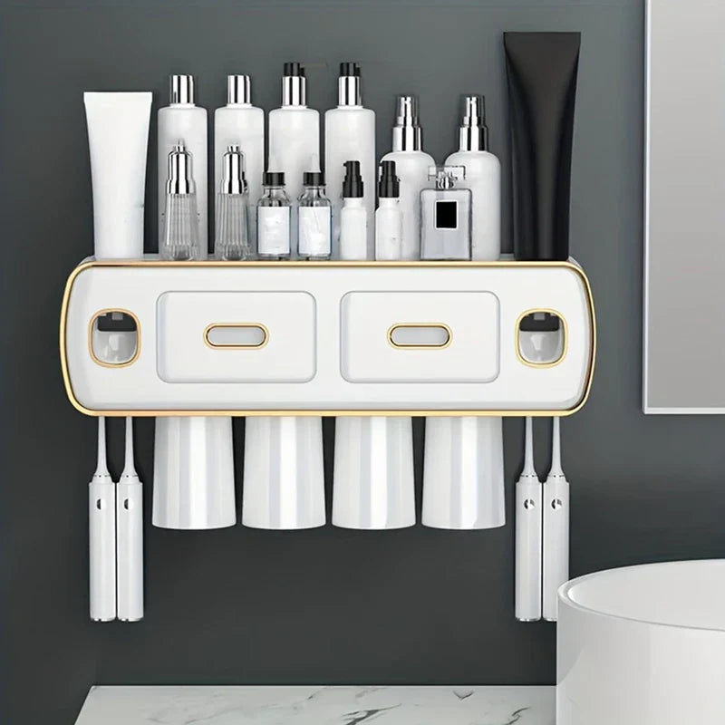 A white wall mount toothbrush holder toothpaste dispenser set mounted on a gray wall, with toiletries on top, hanging cups, and toothbrush slots.