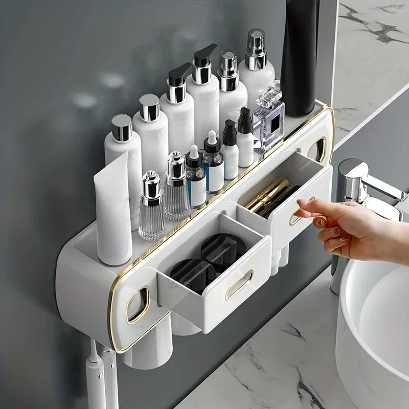 Hand pulling a drawer on a wall mount toothbrush holder toothpaste dispenser set holding skincare bottles above a bathroom sink.