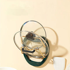 Wall Mounted Pot Lid Holder - Dark green wall-mounted lid holder holding two glass lids, with white kitchen utensils partially visible beside it on a light wall.
