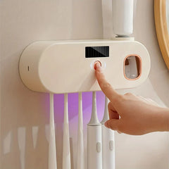 Sanitizador de cepillos de dientes UV - Mano presionando el botón de encendido en un dispositivo de cuidado oral montado en pared de color crema que sostiene múltiples cepillos de dientes eléctricos