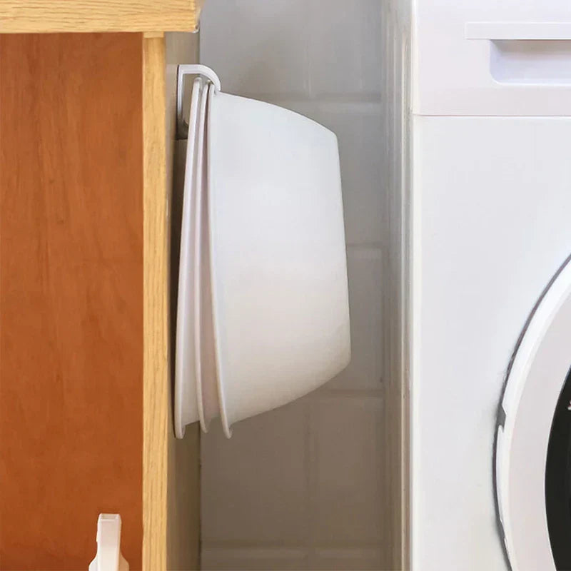 Three folding wash basins hang on a hook between a wood cabinet and a washer, with a wash basin storage rack mounted on the cabinet side.