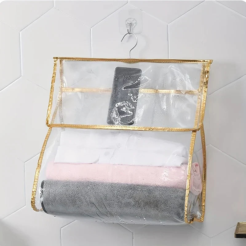 Shower Organizer - Clear gold-trimmed hanging bag holding stacked folded towels and a water-speckled phone, hung on a wall hook