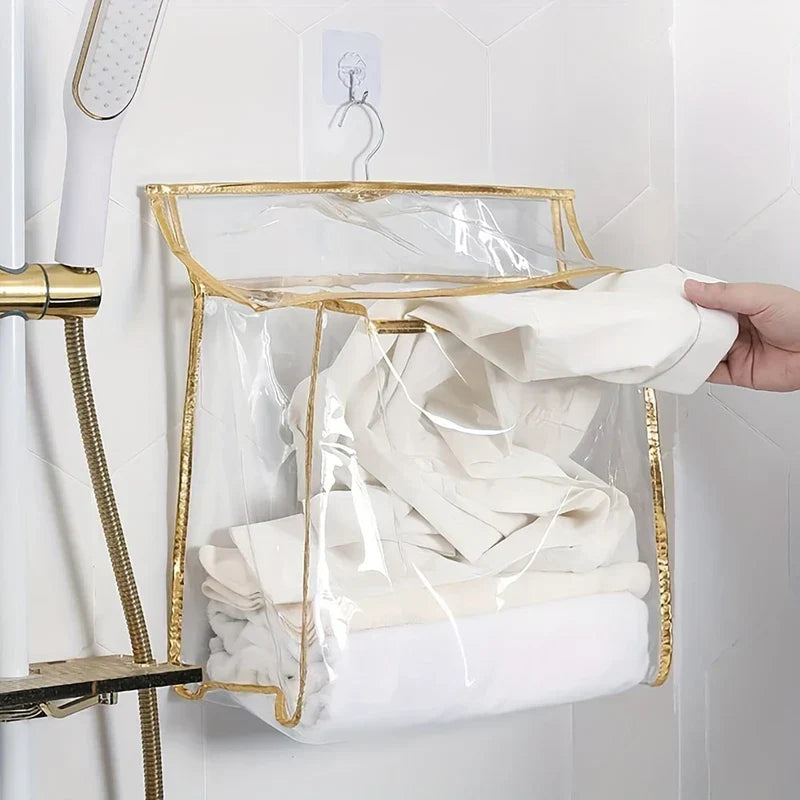 Shower Organizer - Clear hanging storage bag with gold trim hung on a wall hook, as a hand places a white garment into it
