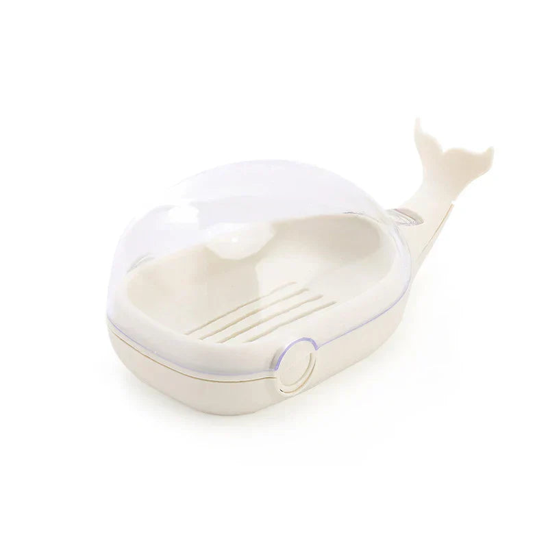 White whale-shaped soap dish with clear flip-top dome lid, raised drain ridges inside, on a plain white background.