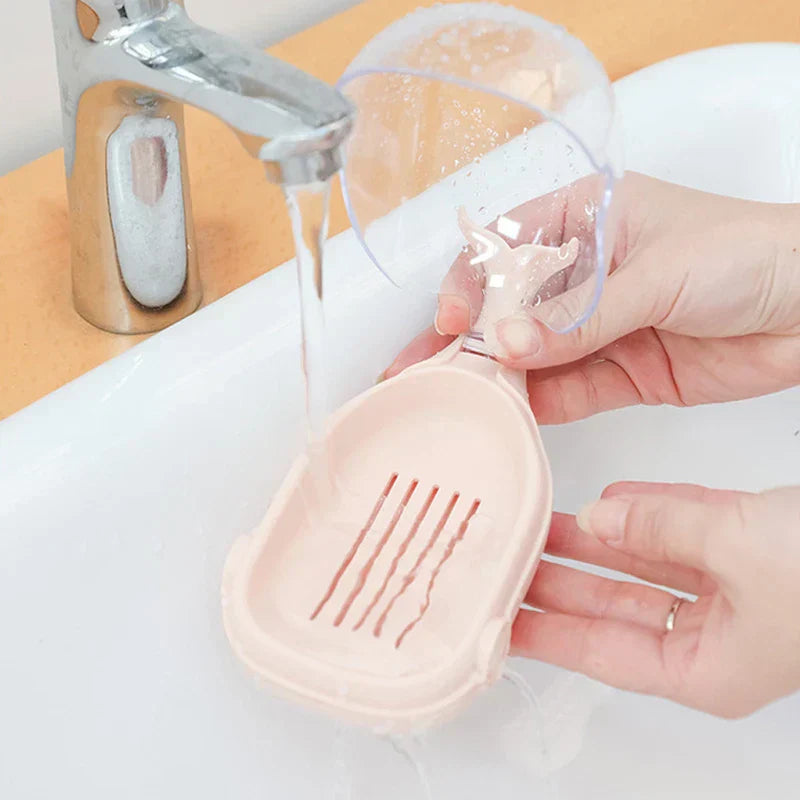 Whale Soap Holder - Hands rinsing a pink whale-shaped plastic soap holder under running water from a faucet over a sink.