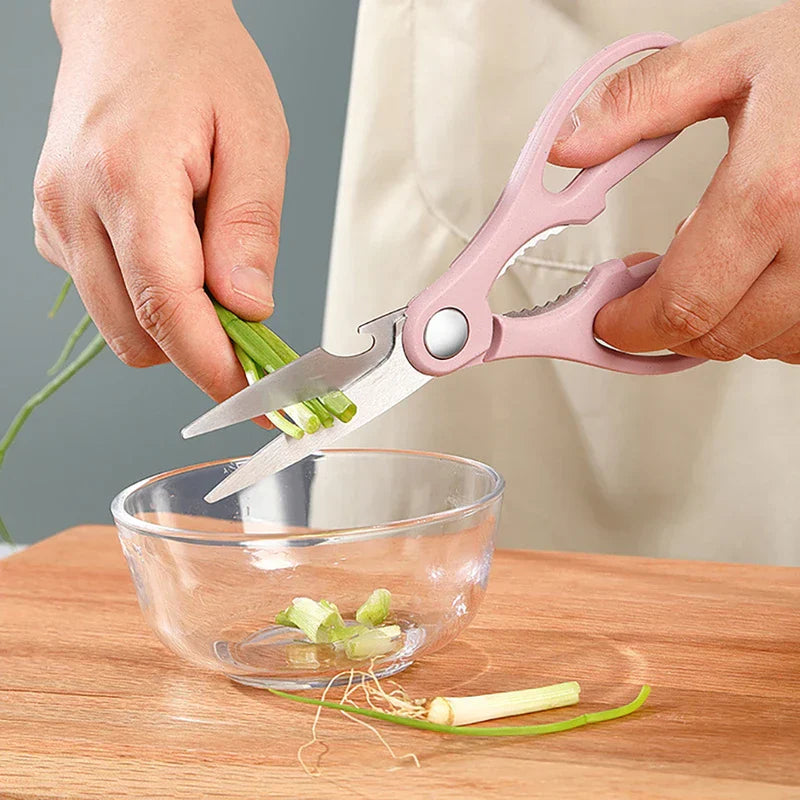 Kitchen Utensil Set - Hands using pink-handled kitchen shears to cut green scallions over a clear glass bowl on a wooden cutting board