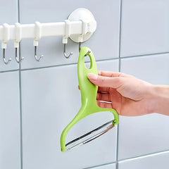 Vegetable Slicer - A hand hangs the green peeler by its handle hole on a suction-cup wall hook rack mounted on gray tile.