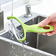 Vegetable Slicer - Hand holding a green vegetable peeler under running tap water over a sink, water splashing.