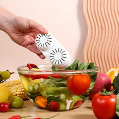 Fruit Vegetable Purifier Washer Capsule - Hand holding the compact produce cleaning device above a glass bowl filled with water and fresh produce