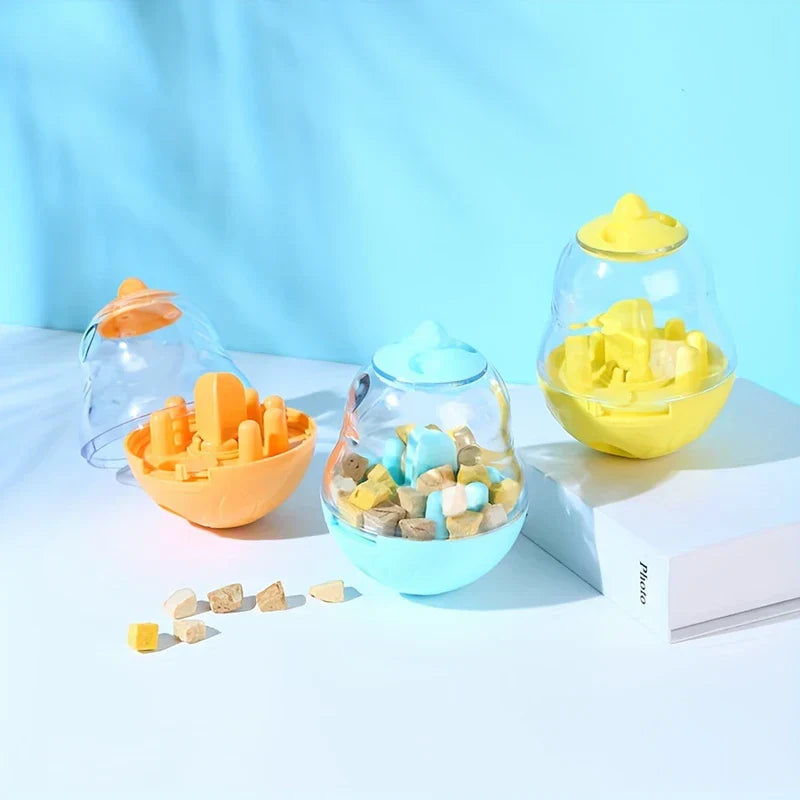 Interactive Pet Toy - Three pear-shaped pet treat toys in orange, light blue, and yellow, with scattered pet treats on a light surface