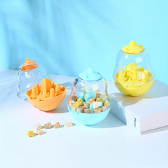 Interactive Pet Toy - Three pear-shaped pet treat toys in orange, light blue, and yellow, with scattered pet treats on a light surface