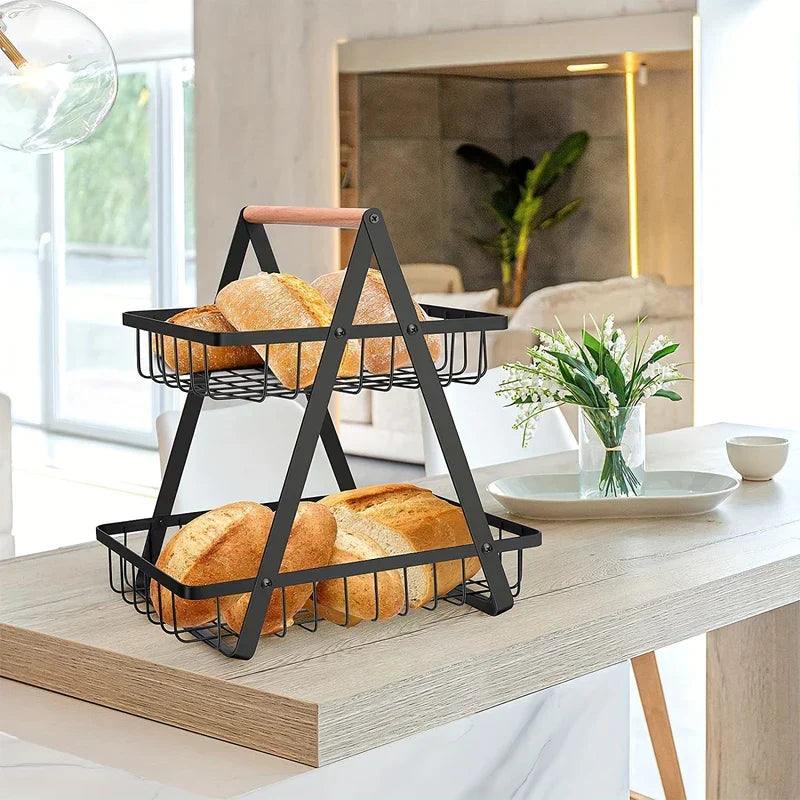Frutero de hierro forjado - Cesta de alambre negro rectangular de dos niveles que sostiene panes, colocada sobre una mesa de comedor de madera clara