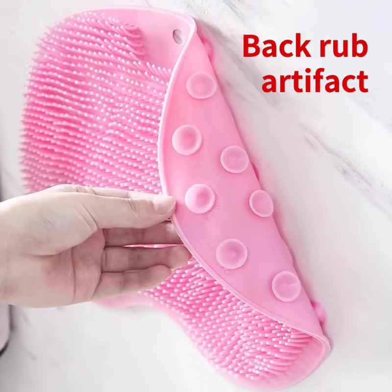 A hand holds a pink silicone shower foot scrubber mat with suction cups and textured bristles, labeled 'Back rub artifact' on a marble surface