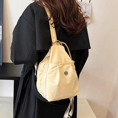 Bolso convertible de hombro: vista trasera de una persona con abrigo negro llevando un bolso convertible cruzado/mochila color crema colgado de un hombro