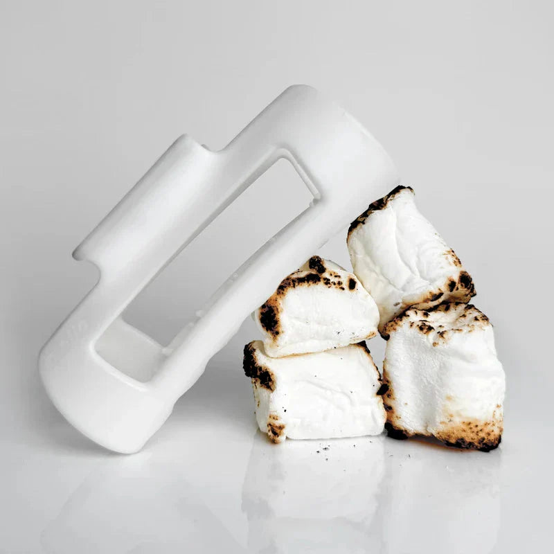 Cloud Clip - White plastic hair clip leaning against a stack of four toasted marshmallows on a reflective white surface
