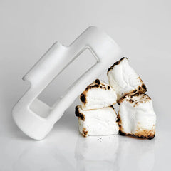 Cloud Clip - White plastic hair clip leaning against a stack of four toasted marshmallows on a reflective white surface