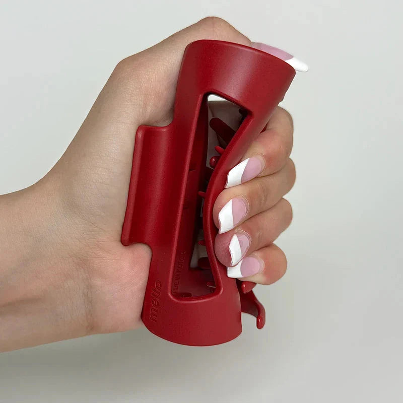 Cloud Clip - Hand holding a closed red hair claw clip, with pink and white French tip fingernails visible.