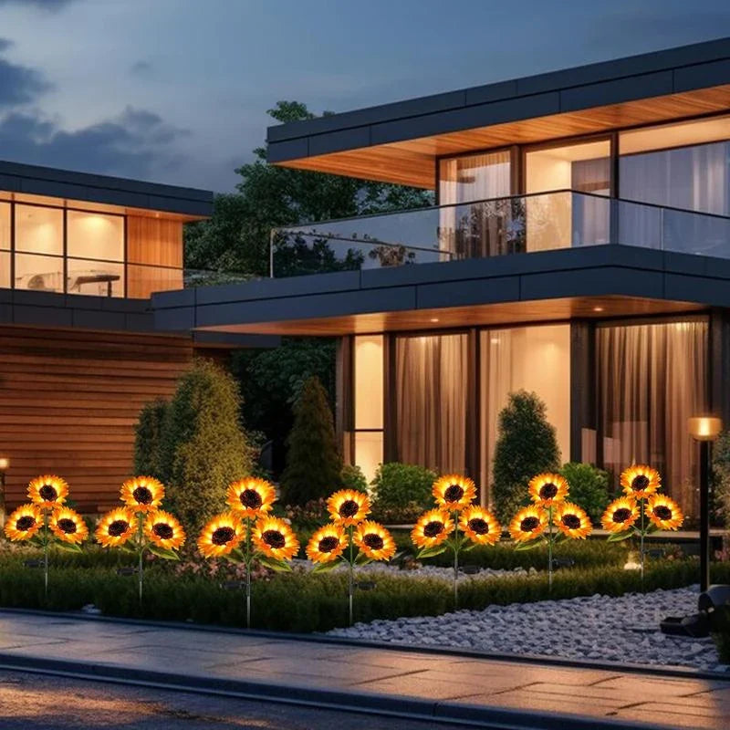 Sunflower Garden Lights - Lit solar sunflower stake lights arranged along the front landscaping of a modern two-story home at dusk