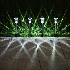 Solar Garden Lights - Four small solar pathway lights glowing at night, placed in grass along square paved tiles casting patterned light shadows