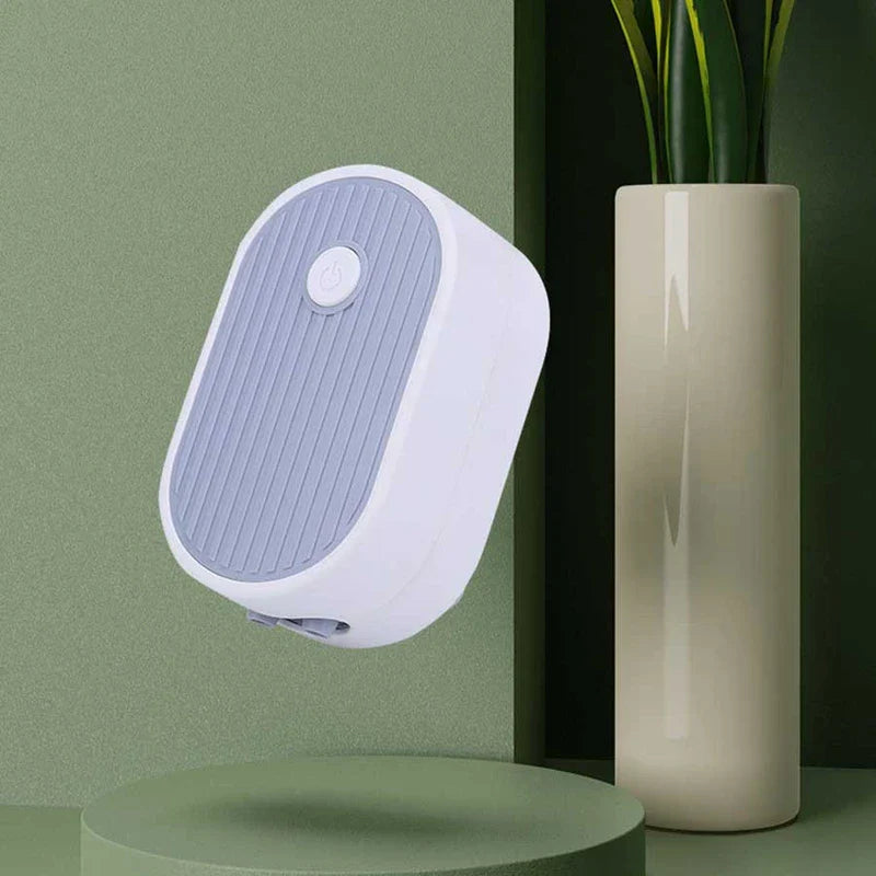 Tubo de drenaje para bandeja de té: pequeño dispositivo electrónico ovalado blanco y azul claro flotando sobre una plataforma redonda verde claro, junto a un jarrón crema con hojas de planta