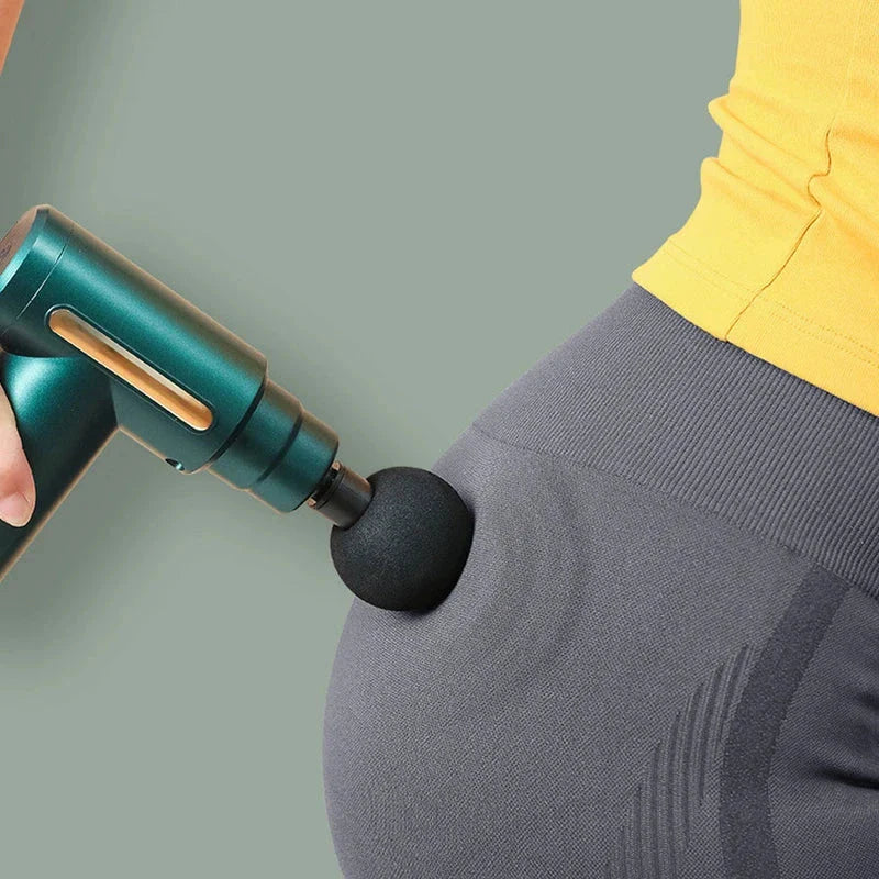 Fascia Gun - Close-up of a teal handheld massage gun with a round black foam head pressed against a person’s hip, over grey leggings and a yellow top