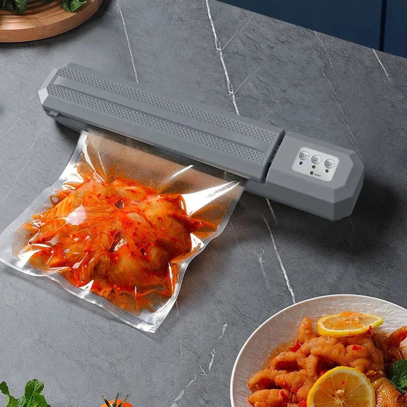 Vacuum Sealer Machine - Gray vacuum sealer sealing a bag of red sauced food, placed on a gray stone countertop with a plated dish nearby