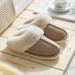 Zapatilla - Zapatilla de casa tipo slip-on en tono taupe cálido con collarín de piel sintética crema y esponjosa, exhibida sobre piso de madera clara