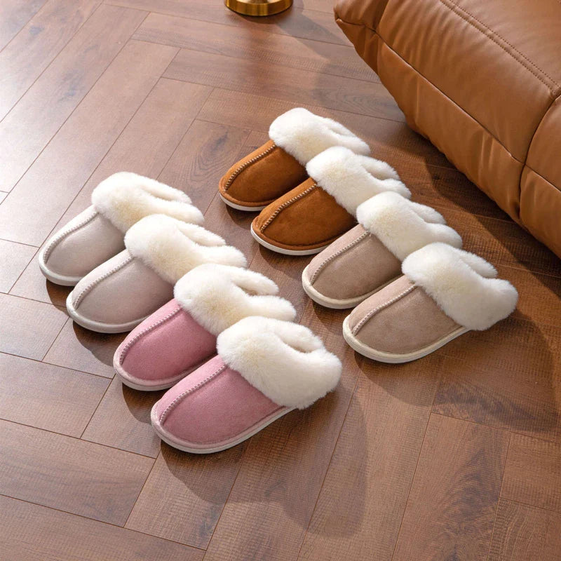 hausschuh - Vier Paar Hausschuhe mit flauschigem Kragen in Hellrosa, Rosa, Sand und Beige auf einem Holzboden neben einem braunen Ledersofa angeordnet