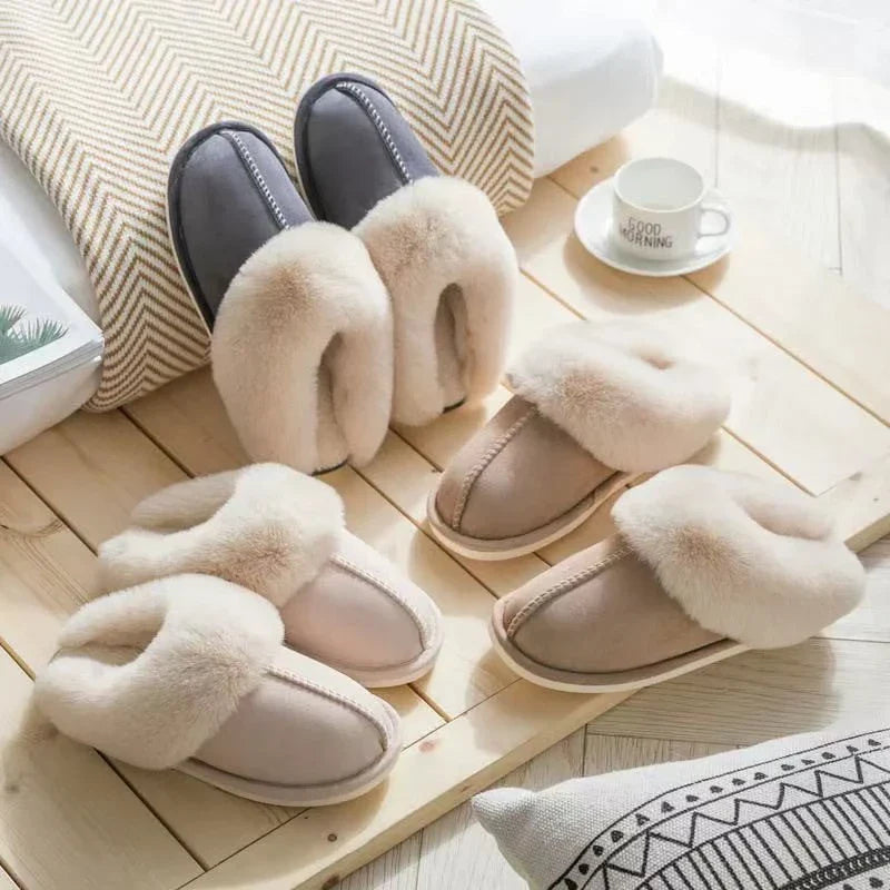 hausschuh - Drei Paar Hausschuhe mit flauschigem Kragen in Grau, Hellrosa und Beige auf einer hellen Holzplatte angeordnet, mit einer Tasse und Kissen in der Nähe