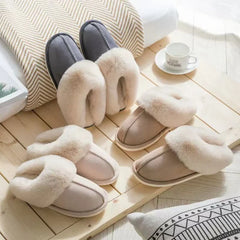 hausschuh - Drei Paar Hausschuhe mit flauschigem Kragen in Grau, Hellrosa und Beige auf einer hellen Holzplatte angeordnet, mit einer Tasse und Kissen in der Nähe