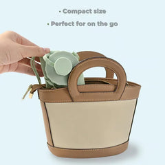 Una mano coloca una botella de agua plegable de silicona verde claro plegada en un bolso pequeño de dos tonos en tostado y beige