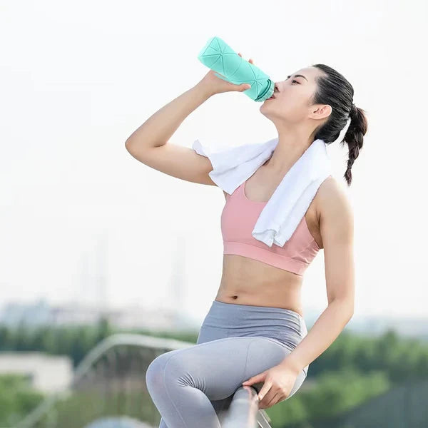 Una mujer con ropa deportiva bebe de una botella de agua plegable de silicona verde claro mientras está sentada al aire libre