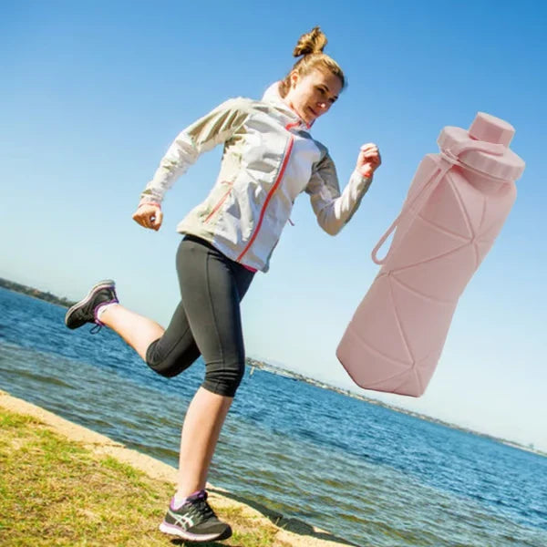 Mujer corriendo junto al agua con una botella de agua plegable de silicona rosa