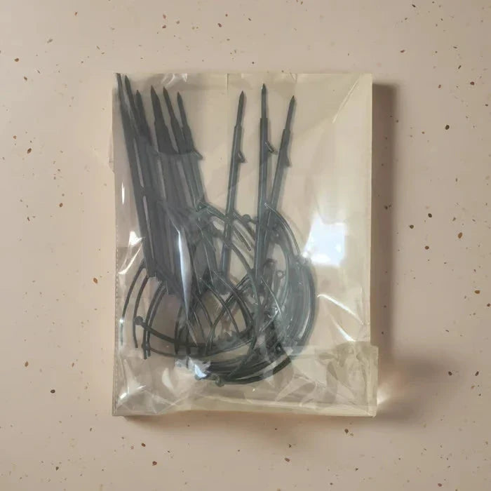 Flat clear plastic bag with dark green plant support stakes inside, laid on a light speckled countertop.
