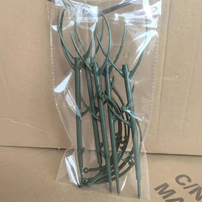 Transparent plastic bag holding multiple dark green branch-shaped plant support stakes, placed on a cardboard surface.